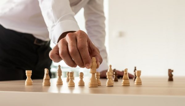 Business leadership concept - businessman standing at his office desk placing chess figures on table with the king in front.